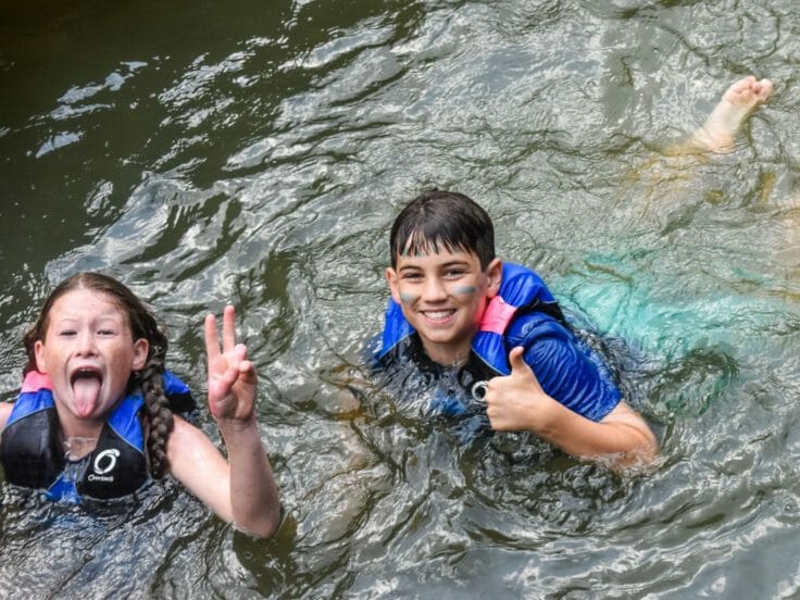 Two campers swimming and giving a thumbs up